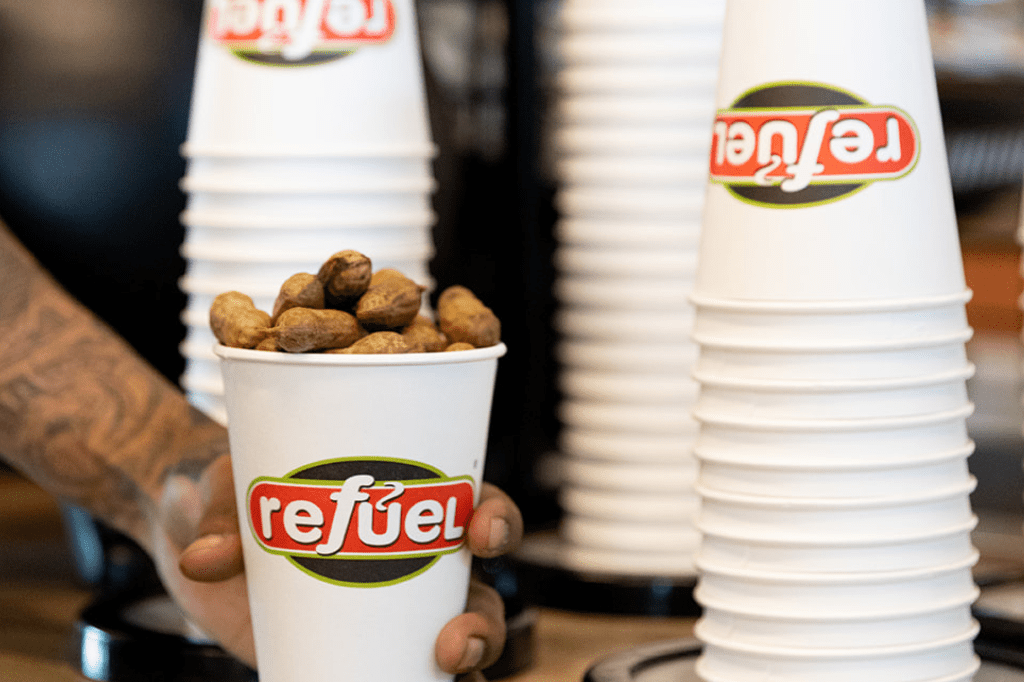Employee arm placing a Refuel cup full of boiled peanuts on a counter next to stacks of Refuel cups.